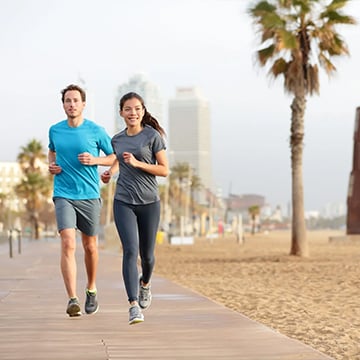 young couple running at sidewalk of the sandy beach