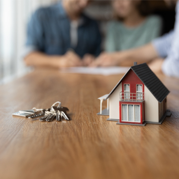 Miniature house and house keys on table while people talk on the background Miniature house and house keys on table while people talk on the background